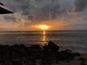 a sunset over the ocean with rocks on the beach at Restu Chalet Tioman in Tioman Island