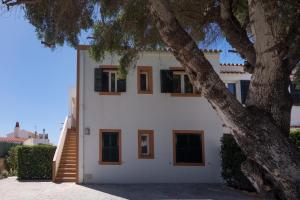 a white house with brown windows and a tree at Llevant 11 E1 in Cala en Bosc