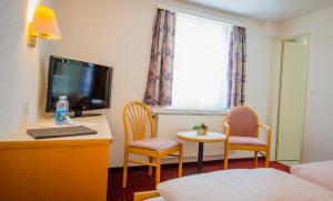 a room with a bed and a tv and a table and chairs at Hotel Heilquelle in Leukerbad