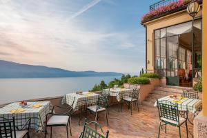 eine Terrasse mit Tischen und Stühlen neben einem Wasserkörper in der Unterkunft Boutique Hotel Villa Sostaga in Gargnano