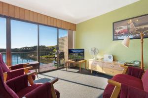 a living room with chairs and a television and a balcony at Pacific Pines Unit 6 in Narooma