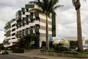 Un edificio con palmeras frente a una calle. en Livramento Palace Hotel, en Vitória da Conquista
