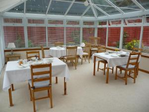 uma sala de jantar com mesas e cadeiras brancas e janelas em Ordieview Bed & Breakfast em Luncarty