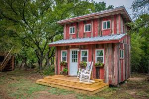 a red tiny house with a porch and a chair at Cozy Cabin Little Red Hen 12 min to Magnolia in Waco