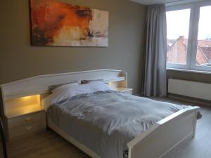 a white bed in a bedroom with a window at BelArté framing shop, spacious apartment with garage in the heart of Ieper in Ieper