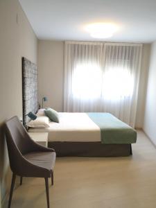 a bedroom with a bed and a chair and a window at Apartamentos Real Lleida in Lleida