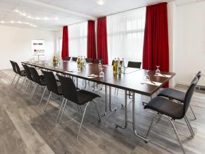 DORMERO Hotel Hannover-Langenhagen Airport في هانوفر: قاعة اجتماعات كبيرة مع طاولة وكراسي طويلة