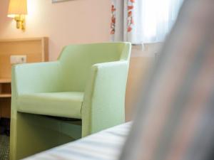 a green chair sitting next to a bed in a room at Gästehaus Mönchshof in Sommerhausen