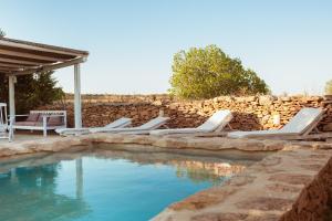 a swimming pool with lounge chairs and a stone wall at Casa Mayo in Sant Francesc Xavier