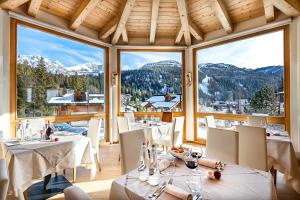 um restaurante com mesas e cadeiras e janelas grandes em Hotel Dahu em Madonna di Campiglio