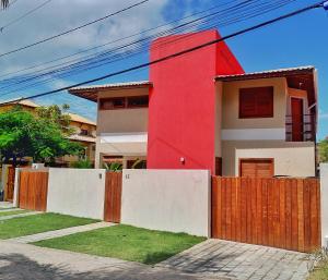 ein rotes Haus mit einem Zaun davor in der Unterkunft Corvina Suites in Praia do Forte