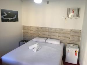 a small bedroom with a white bed and a refrigerator at Pousada Poleto's in Bertioga
