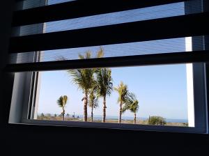 una ventana con vistas a una playa con palmeras en Cerritos Apartamento en Mazatlán