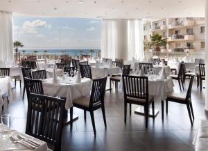 a restaurant with white tables and chairs and the ocean at Capital Coast Resort And Spa in Paphos