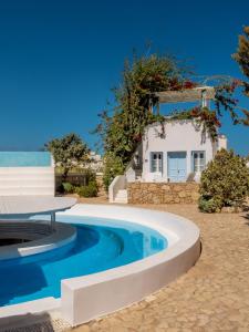 a pool with a table and a house in the background at Chora Resort Hotel & Spa in Chora Folegandros