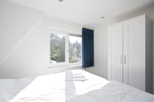 a white bedroom with a bed and a window at Bok's Bungalowpark in Garderen
