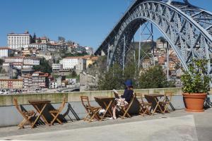 Porto View by Patio 25 في فيلا نوفا دي غايا: امرأة تجلس على طاولة أمام جسر