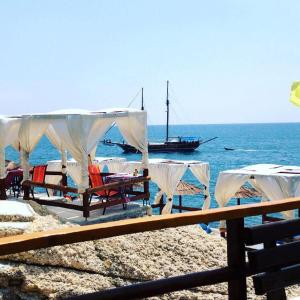 a group of tables and chairs on a beach with a boat at Sunset Old Town in Ulcinj