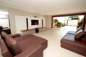 a living room with a brown leather couch and a television at Raru's Motel Via Costeira (Adult Only) in Natal