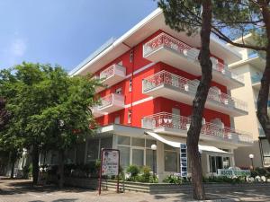 a red building with white balconies and a sign in front of it at Ciccio Hotel in Misano Adriatico