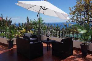 einen Balkon mit Stühlen, einem Tisch und einem Sonnenschirm in der Unterkunft Tabua Village in Ribeira Brava