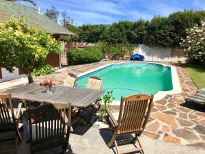 una mesa de madera y sillas junto a una piscina en African Holiday home in Table View, en Ciudad del Cabo