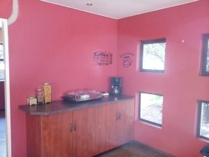 a room with a red wall with a kitchen with a counter at Woodpecker Guesthouse Middelburg Mpumalanga in Middelburg