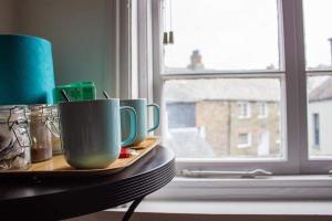 a tray with three cups on a table next to a window at Drang house all rooms have stairs in Padstow