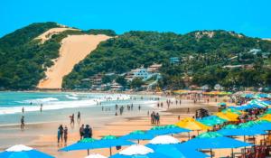 a crowded beach with blue and yellow umbrellas and people at Porto Tropical Residence in Natal