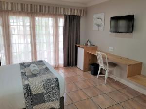 a room with a bed and a desk and a television at Shonalanga Lodge in Vryheid