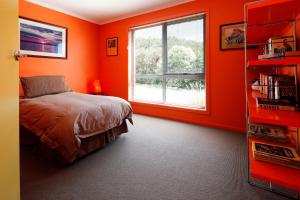Schlafzimmer mit orangefarbenen Wänden, einem Bett und einem Fenster in der Unterkunft Sisters Beach Retreat in Sisters Beach