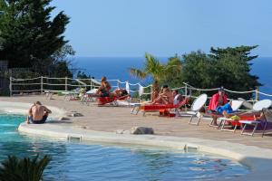 a group of people sitting around a swimming pool at Baglio Dello Zingaro in Scopello