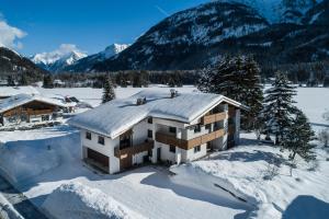 een huis bedekt met sneeuw met bergen op de achtergrond bij Ferienwohnungen stiLECHt in Elbigenalp