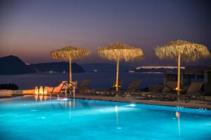 a pool with umbrellas and chairs and the ocean at night at Sunset Faros in Akrotiri