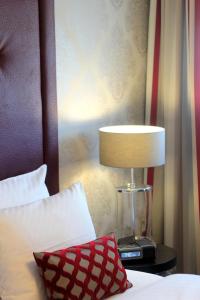 a bed with a red pillow and a lamp on a table at Parkhotel Heidehof Long Stay in Ingolstadt