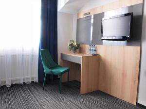 a room with a desk with a tv and a green chair at Hotel Duet in Człuchów