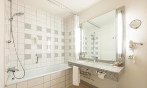 a bathroom with a tub and a sink and a mirror at Mercure Hotel am Messeplatz Offenburg in Offenburg