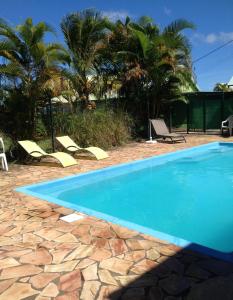 a blue swimming pool with chairs and palm trees at Les Vanilliers Location BUNGALOWS in Saint-Joseph