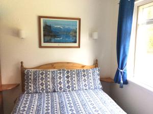 a bed with a blue and white comforter and a window at Dalkell Cottage in Tyndrum