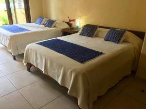 2 Betten in einem Zimmer mit blauen Kissen darauf in der Unterkunft Un Escondite Mágico in Barra de Potosi