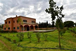 a large brick building in a field with trees at Villa Moderne dans la Ferme "Belkheir" avec Piscine, Chevaux et Aire de Jeux pour Enfants in Berrechid