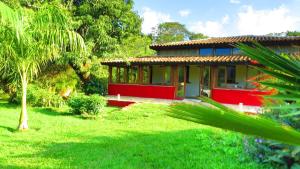 uma casa vermelha e amarela num jardim verde em Praia da Crioula em Vargem Bonita