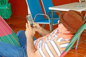 Ein Mann, der auf einem Stuhl sitzt und ein Handy benutzt. in der Unterkunft Hostal Augustos in San Juan del Sur