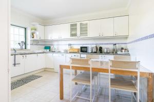 Liv In Ericeira Guest House في إيريسييرا: مطبخ بدولاب بيضاء وطاولة خشبية