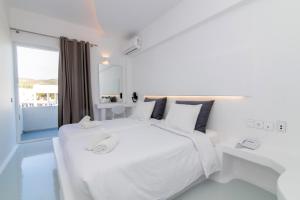 a white bedroom with a large white bed and a window at Byzantio City Hotel in Tinos