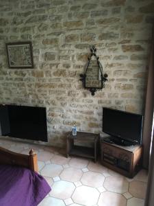 1 dormitorio con pared de piedra, TV y mesa. en La Luterne en Villaines-les-Prévôtes