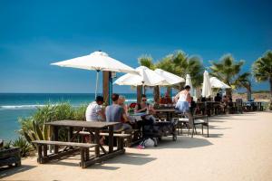 ludzie siedzący przy stołach na plaży pod parasolami w obiekcie Apartamento Oropendola 9 w mieście El Puerto de Santa María