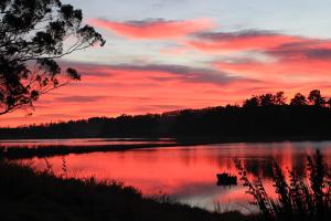 a sunset over a lake with a boat in it at The Bird Hide - rustic luxury by the water in Dunedin