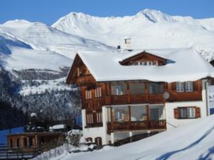 une maison dans la neige avec des montagnes en arrière-plan dans l'établissement Sertig Ferienwohnung, à Davos