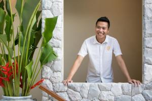 un hombre con una camisa blanca de pie detrás de una pared de piedra en Moonstone - Samui's Premier Private Villa en Bang Rak Beach